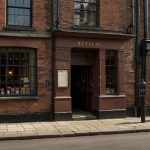 An old brick building in Bristol’s Union Street, once home to J.S. Fry & Sons’ factory, with a vintage sign displaying “Chocolat Delicieux à Manger” amidst a bustling 19th-century street scene.