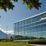 A sleek, modern building with glass windows and the Nestlé logo, surrounded by lush greenery under a clear sky in Vevey, Switzerland.