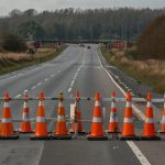 Traffic sign indicating closure of the slip road from A120 to A133 with red and white barriers and cones on a sunny day