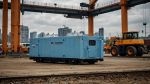 A sleek hydrogen fuel cell generator, the Hitachi HyFlex, sits prominently on a bustling Rotterdam construction site, surrounded by electric machinery and workers, showcasing a zero-emission future for the industry.