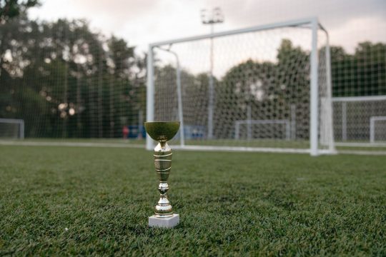 A football trophy standing on the grass in front of a goal