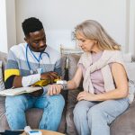 Healthcare professional checking the blood pressure of an elderly woman seated on a sofa at home